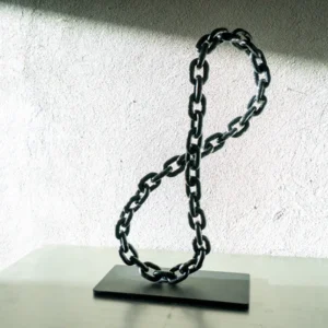A vertical, infinity-shaped sculpture made from a heavy black metal chain, standing on a sleek rectangular metal base.